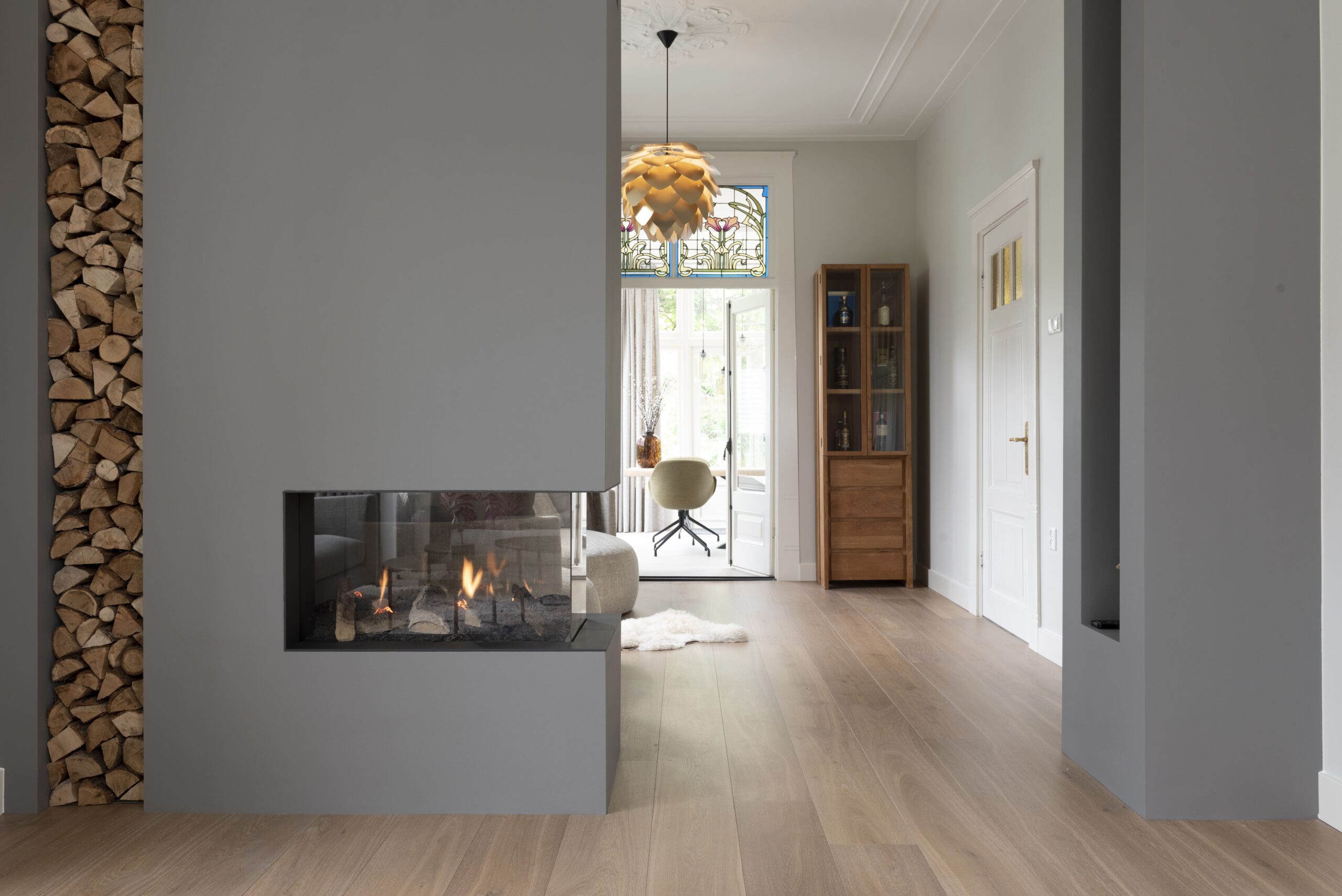 Moderne woonkamer met grijze haard en doorkijk naar serre in gerenoveerd herenhuis in Nijmegen.